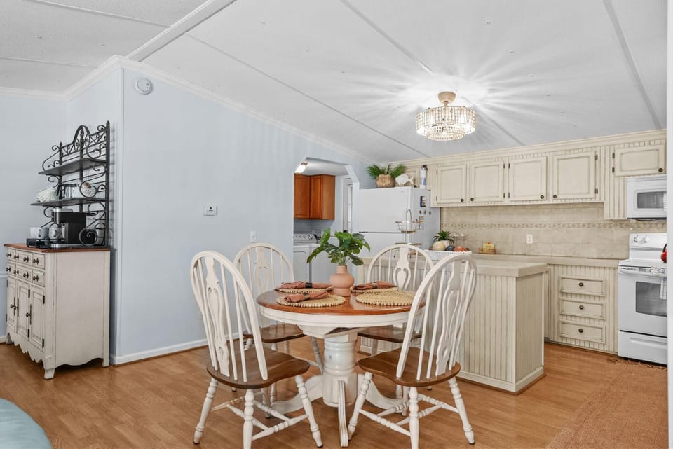 Dining area features a round wood table with four white spindle-back chairs under a crystal ceiling light.