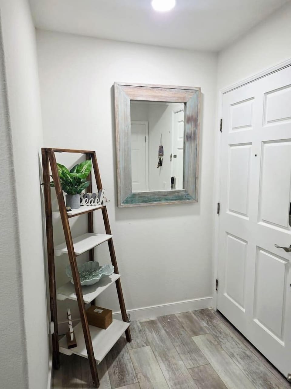 Step through the door into a bright, breezy entryway that instantly sets a relaxed beach-vacation tone. Soft white walls reflect natural light from the ceiling fixture, creating an airy and open feel in this compact, welcoming space.