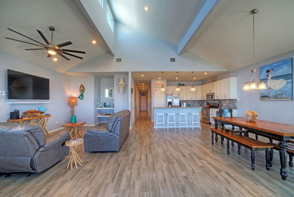 Bright, open-concept great room with vaulted ceilings, big-screen TV, and a spacious kitchen and dining area for gathering.
