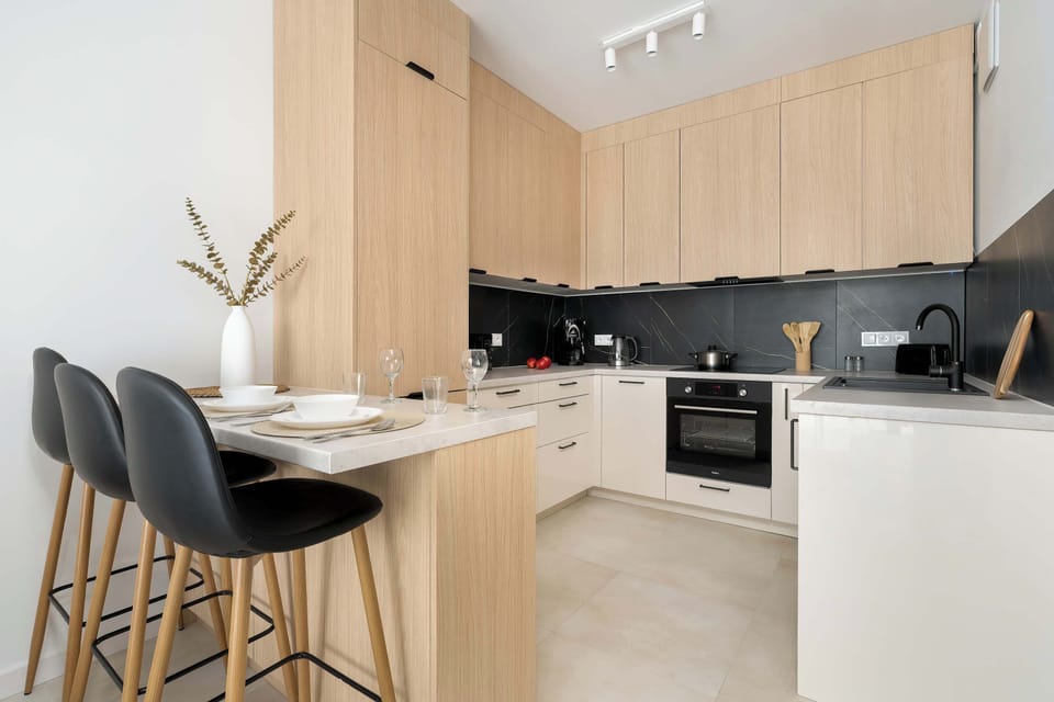 A breakfast bar with three black stools offers a convenient dining option within the open-plan space. The kitchenette behind it is finished with high-quality materials and contemporary appliances.