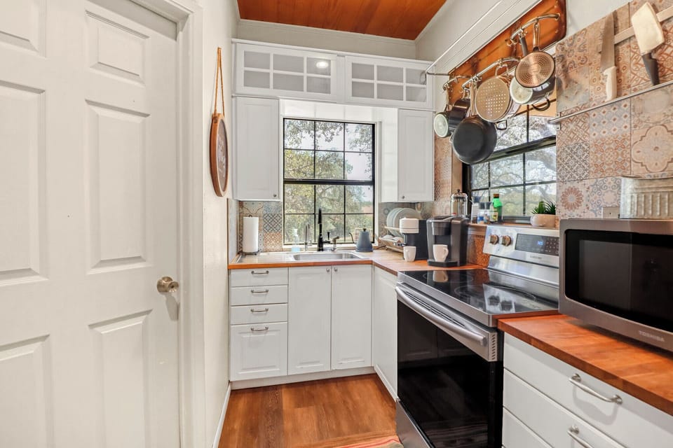 Picture yourself preparing meals in this charming kitchen, where warm wood tones meet crisp white cabinetry and sunlight streams through garden-view windows, creating your perfect home-away-from-home cooking space.