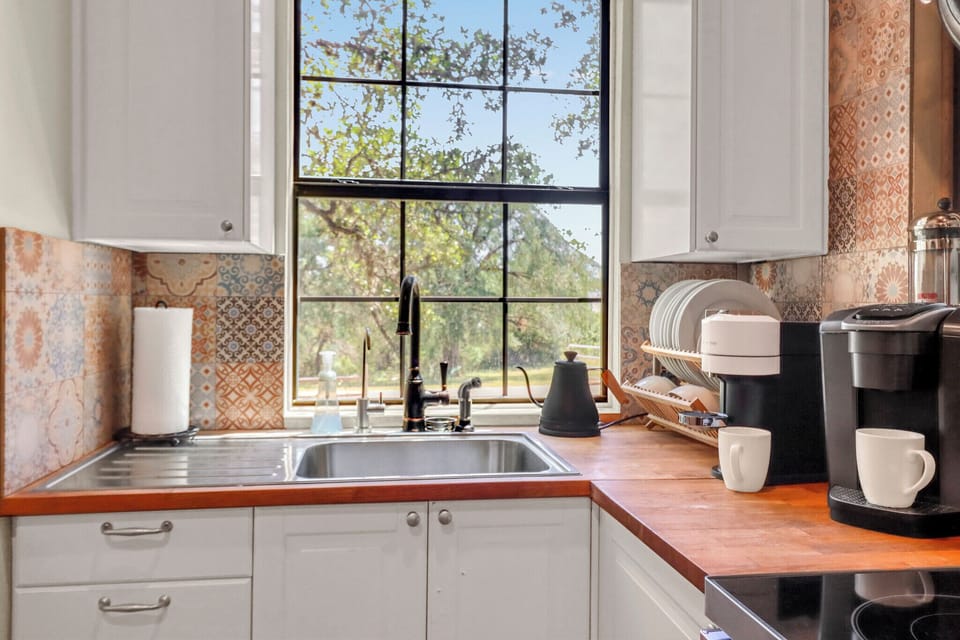 Your fully equipped kitchen looks out to peaceful garden views, with warm wood counters and patterned tile backsplash adding character. Fresh coffee awaits you each morning.