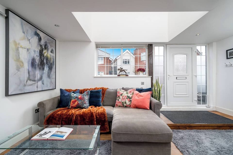 Inviting living area with a large sectional sofa adorned with colorful pillows and a warm throw. A skylight and front window fill the space with natural light, while a glass coffee table and bold wall art add modern flair. A welcoming entrance  