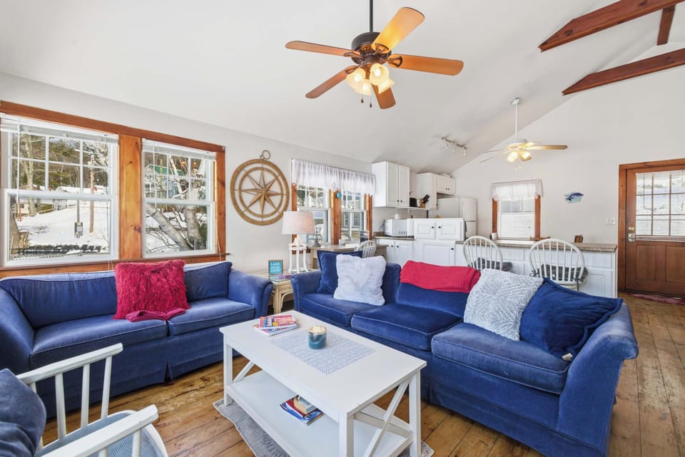 The vaulted ceiling and exposed wood beams give the living room an open, airy feel, with the lake visible through the windows on both sides.