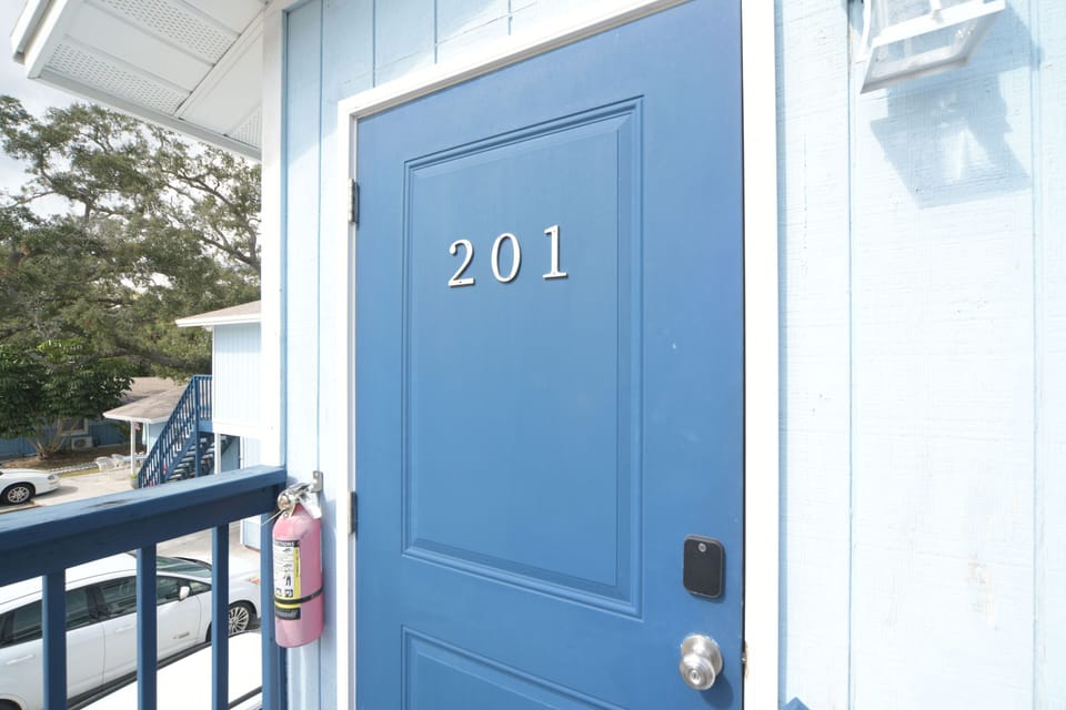 Blue door marked “201” opens to the apartment’s private entryway with a nearby fire extinguisher.