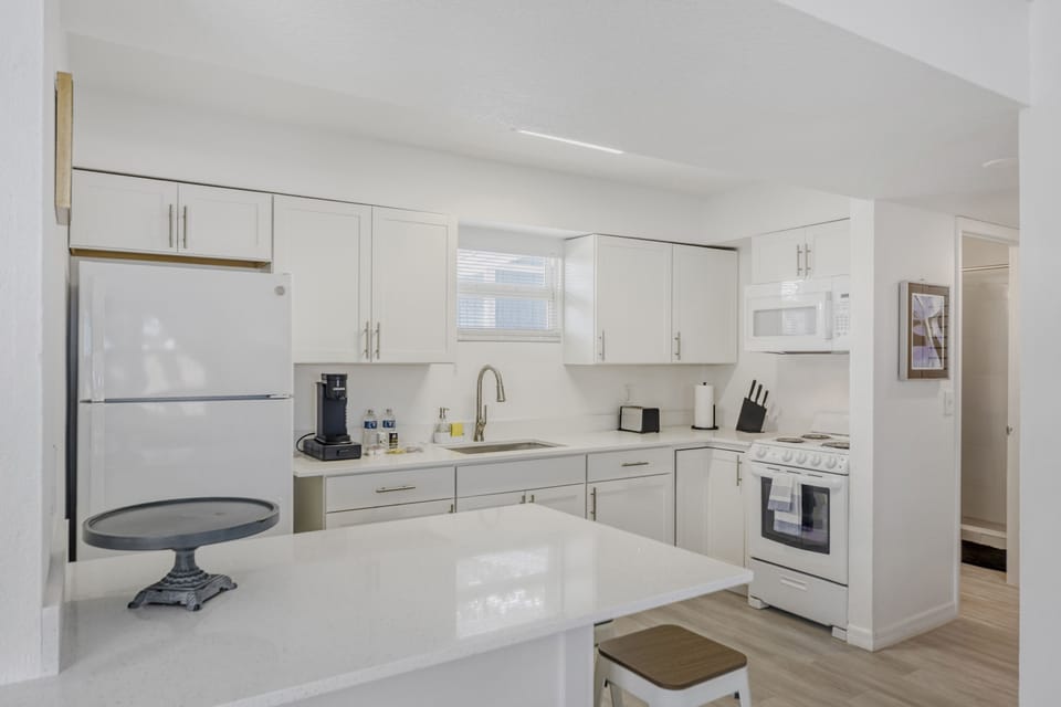 Bright modern kitchenette with white cabinetry, full-size appliances, and a spacious island counter.