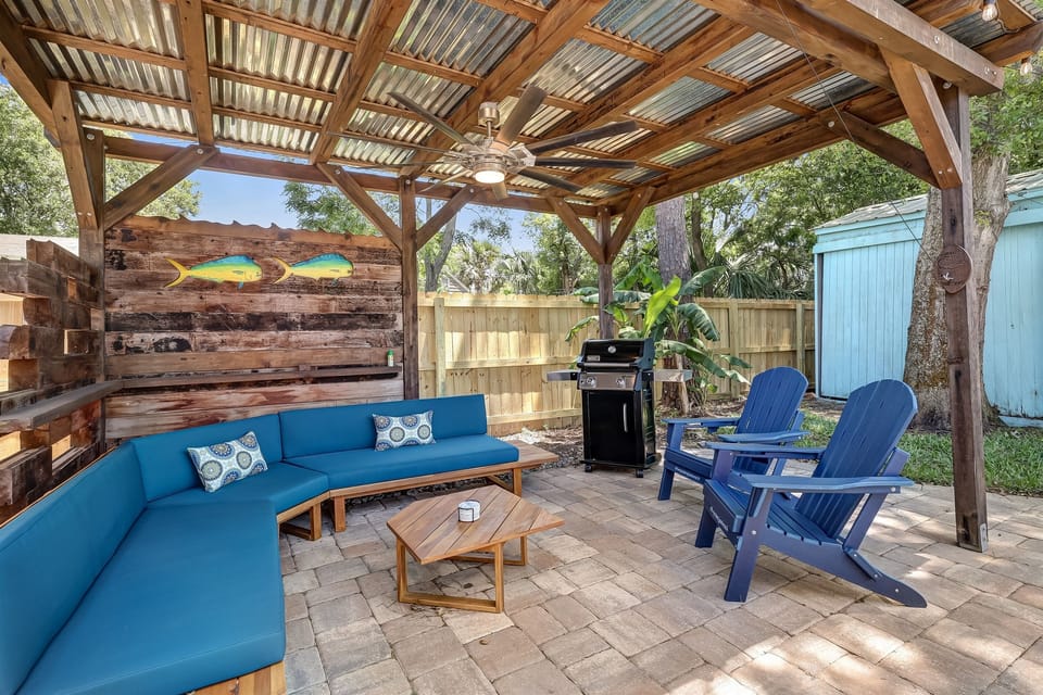 Covered pergola lounge with sectional seating, grill, and outdoor fan.