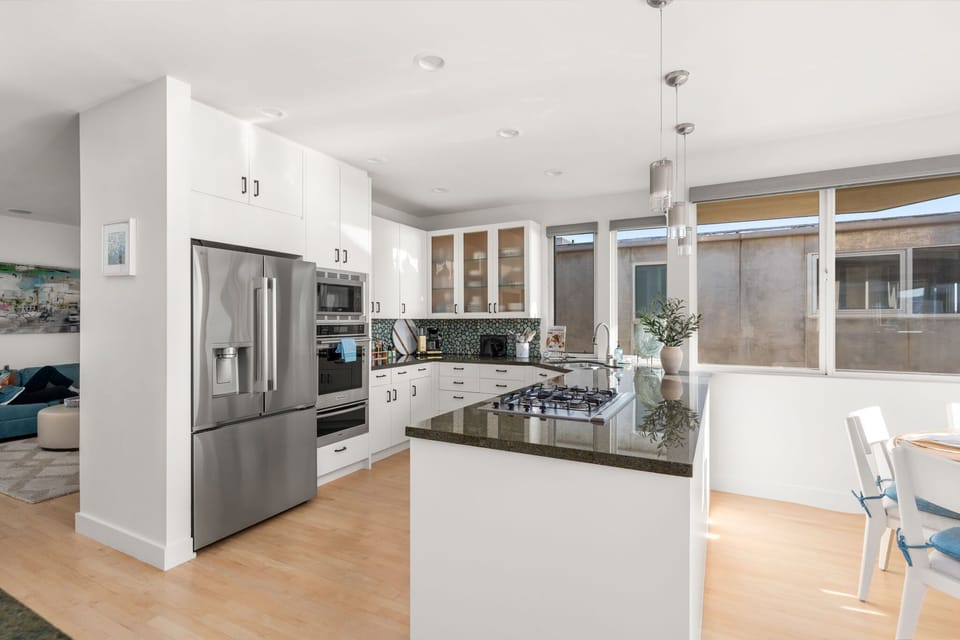 Bright open kitchen with stone countertops, stainless steel appliances, and a large island designed for gathering, cooking, and easy conversation.