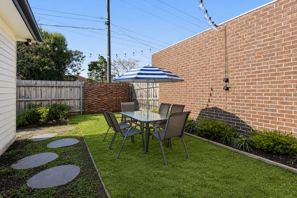 Fenced backyard with dining set, umbrella, and twinkling string lights