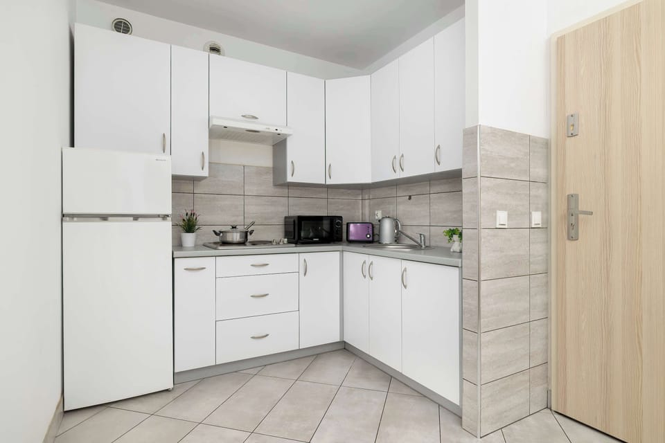 The functional kitchen is equipped with white cabinetry, a refrigerator, and essential household appliances. Light tiles on the floor and walls give the room a sterile, clean appearance.