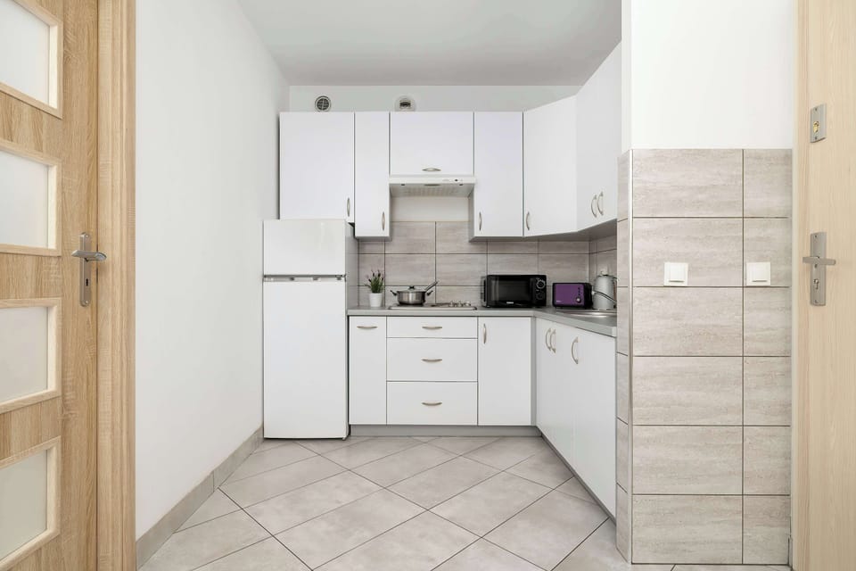 The kitchen viewed from a different perspective showcases white cabinet fronts with sleek metal handles. There is ample workspace on the countertop, and a microwave is tucked into the corner.