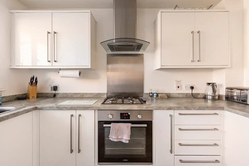 This modern kitchen blends form and function with a gas cooktop, stainless steel oven, and chic white cabinets. Thoughtful details and sleek finishes make cooking a pleasure.
