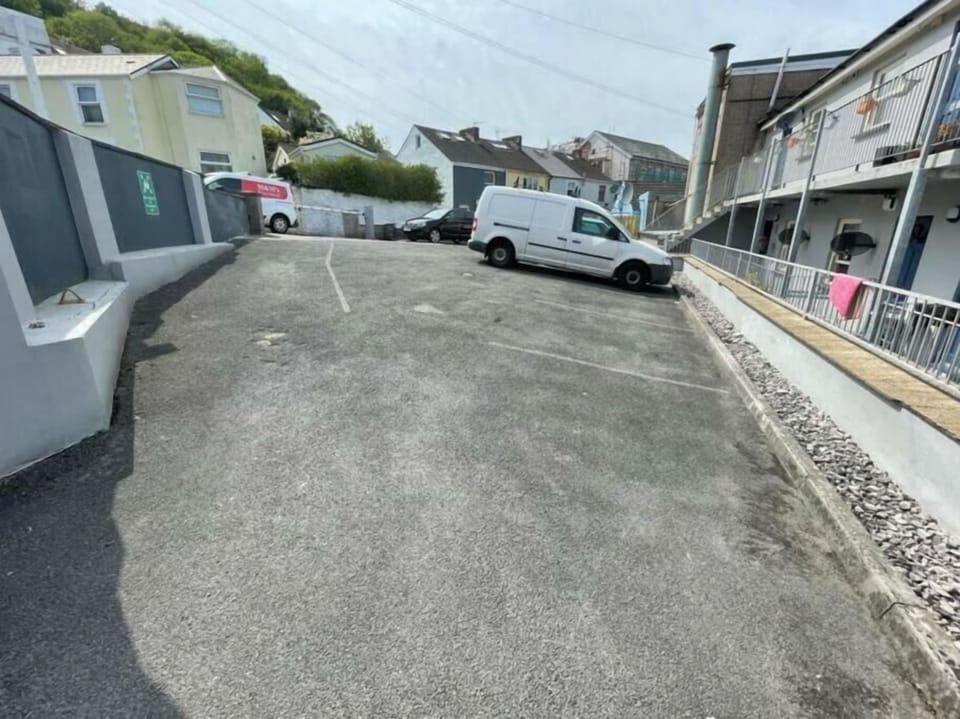 A neat paved parking area with faint lines and a white van parked centrally. Surrounded by buildings and a railing, the space offers guests a straightforward, functional spot for vehicle access.