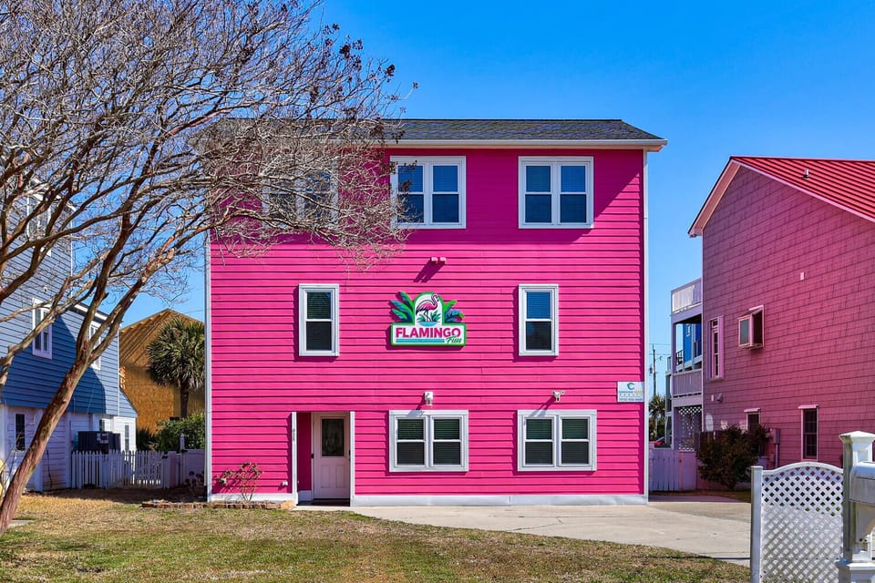 Bright pink vacation rental building with colorful signage creates a cheerful beachside atmosphere in this coastal neighborhood.