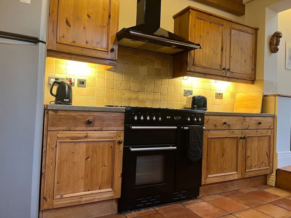 The kitchen is set up for cooking with a large black range oven, extractor hood, fitted pine cabinets, and a tiled splashback.