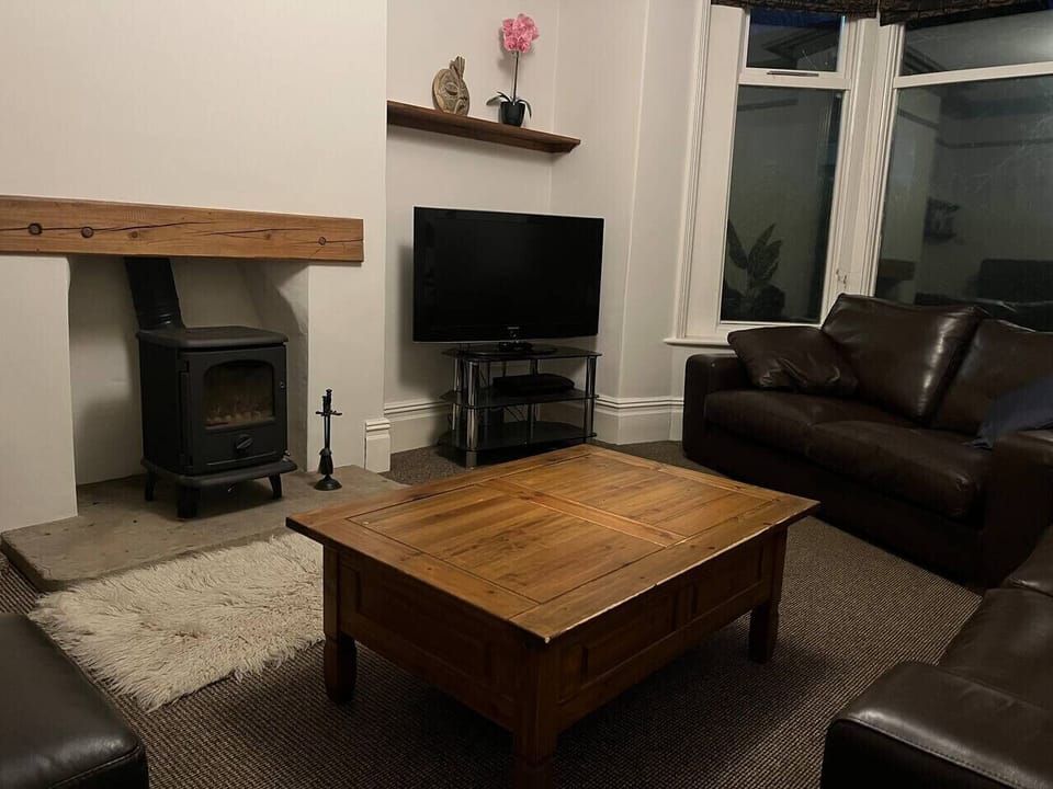 Guests can settle into the lounge, which features two dark leather sofas arranged around a wood-burning stove with a TV mounted above.