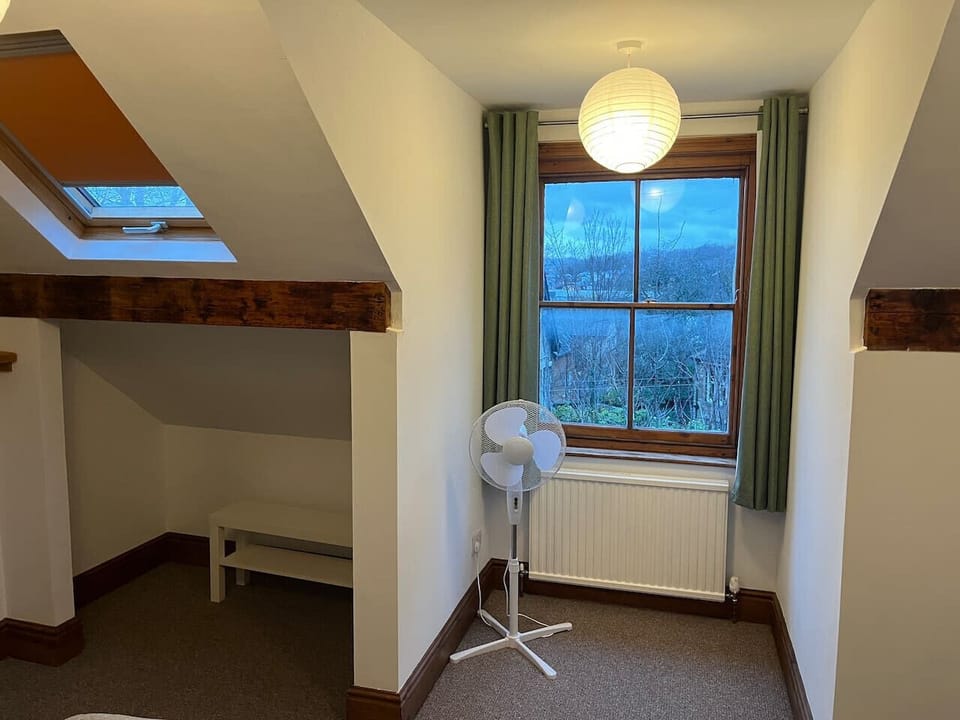 Attic room with a sloped ceiling, Velux skylight, exposed timber beam, a desk, chair, and a portable fan on the floor.