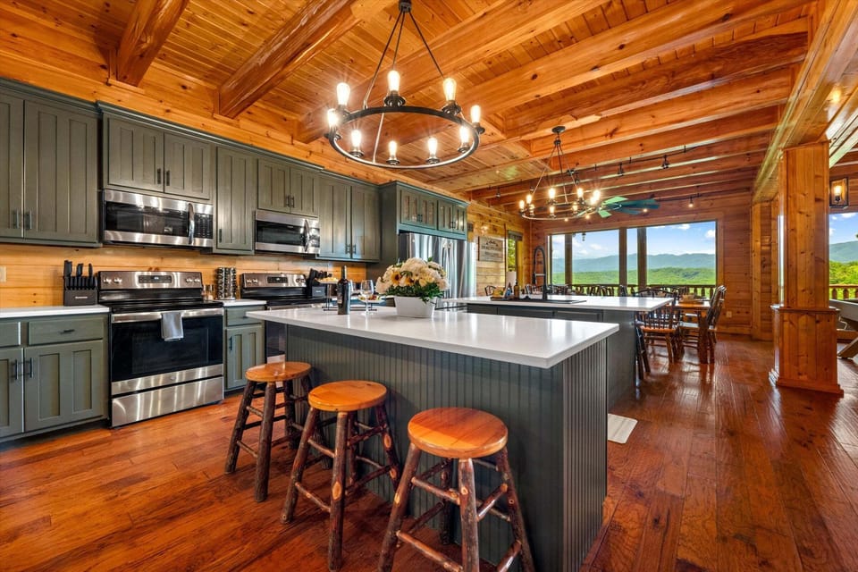 Cabin living room with pool table, stone fireplace, mounted TV, leather lounge chairs, and scenic mountain views through glass doors.