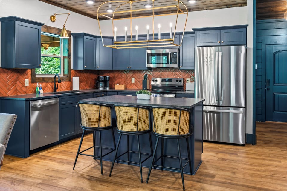 Stunning kitchen featuring deep blue cabinetry, copper-toned herringbone backsplash, stainless steel appliances, and island seating at Blue Bird cabin in the Great Smoky Mountains, Tennessee