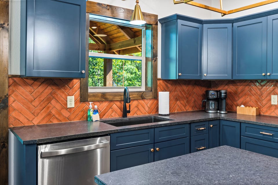 Modern kitchen with stainless steel refrigerator, dishwasher, copper backsplash, and bold blue cabinetry at Blue Bird three-bedroom Smoky Mountain cabin, Tennessee
