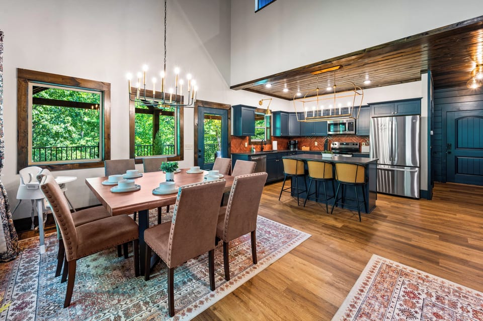 Open concept kitchen and dining area with blue cabinetry, copper backsplash, chandelier, and dining table for eight at Blue Bird three-level cabin in the Smoky Mountains, Tennessee