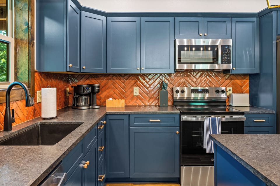 Kitchen corner featuring stainless steel stove, deep blue cabinetry, copper herringbone backsplash, and coffee maker at Blue Bird cabin in the Great Smoky Mountains, Tennessee