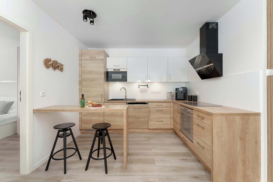 The kitchenette is designed in a modern style with wood-effect cabinetry and sleek black accents, including a chimney hood. It is fully equipped with high-end appliances like an oven and induction hob.