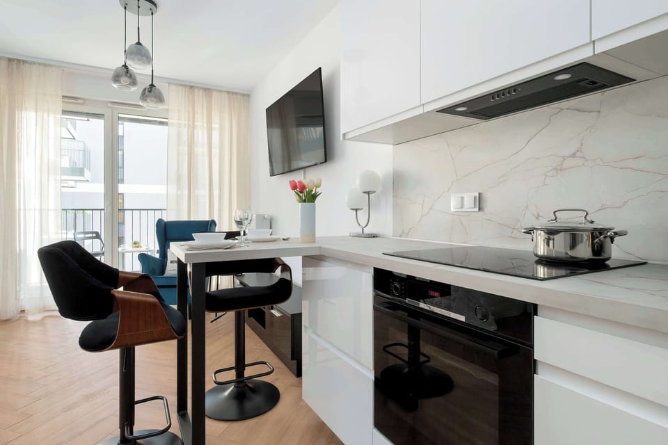 A spacious kitchen with a dining area is shown here. It has a modern white kitchen counter and also a dining counter where two people can comfortably sit.