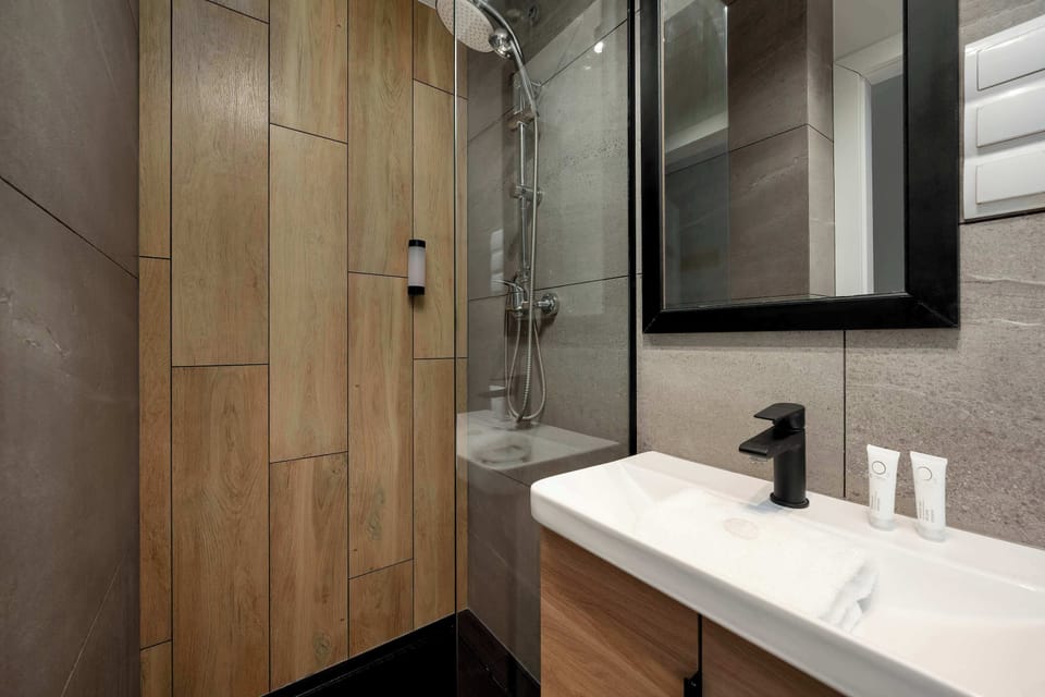 Another bathroom angle showing a sink, mirror, and a wooden cabinet door nearby. Neutral-colored tiles cover the walls. The layout looks compact and well organized.