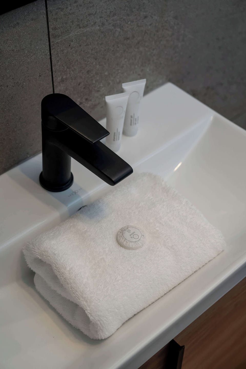 A close-up of a small bathroom sink with a black faucet. The white basin contrasts with the darker hardware.