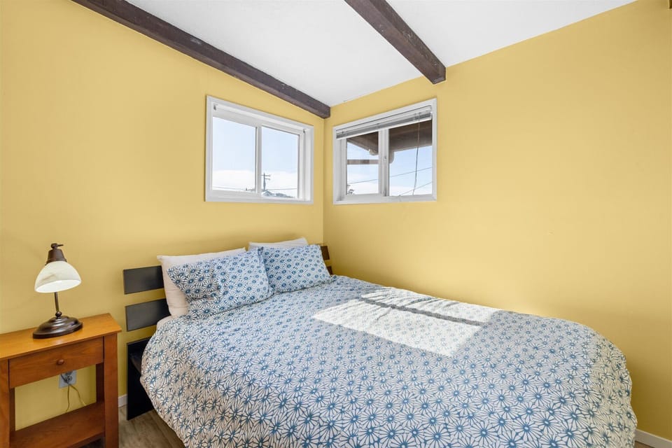 Drift off in your cozy bedroom featuring exposed beams, sunshine-yellow walls, and patterned bedding that creates the perfect retreat.