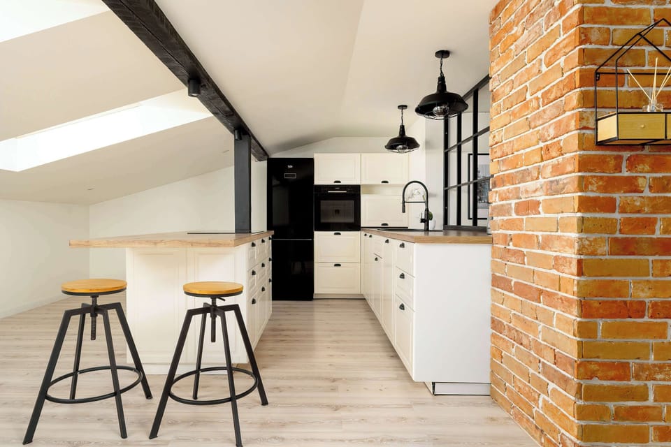 A sleek kitchen view captures the white cabinetry and light wood countertops under a skylight. Two black bar stools are positioned at the island, perfect for a quick breakfast.