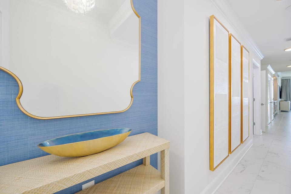 Decorative blue wall and gold-framed mirror reflect the hallway's calm coastal style as you arrive
