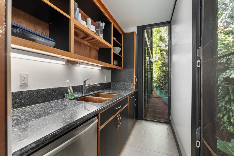 Cook with ease in this sleek modern kitchen featuring granite counters, wood cabinetry, and garden views through sliding doors.