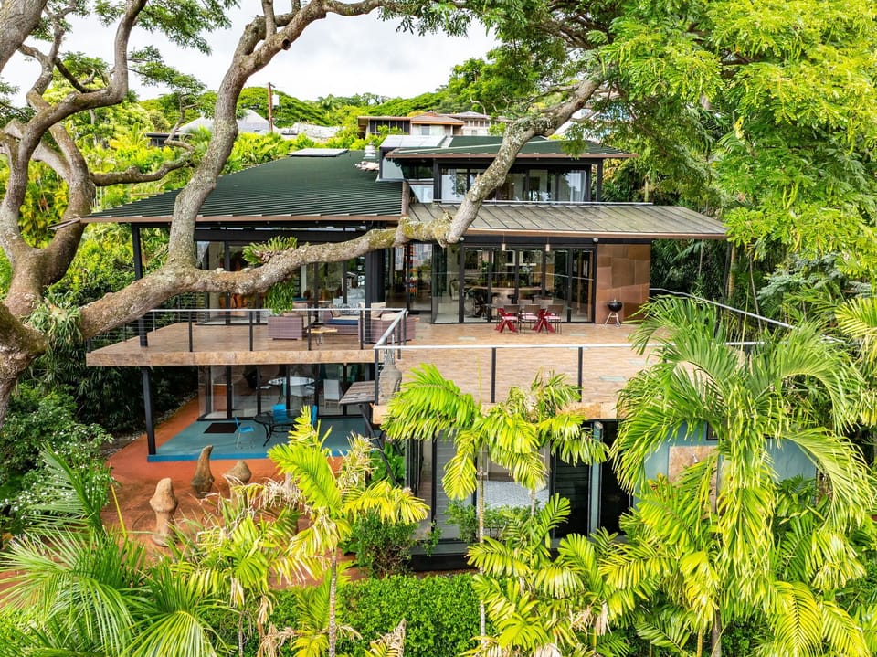 Modern tropical villa nestled among lush vegetation with multiple levels and expansive outdoor lanai.