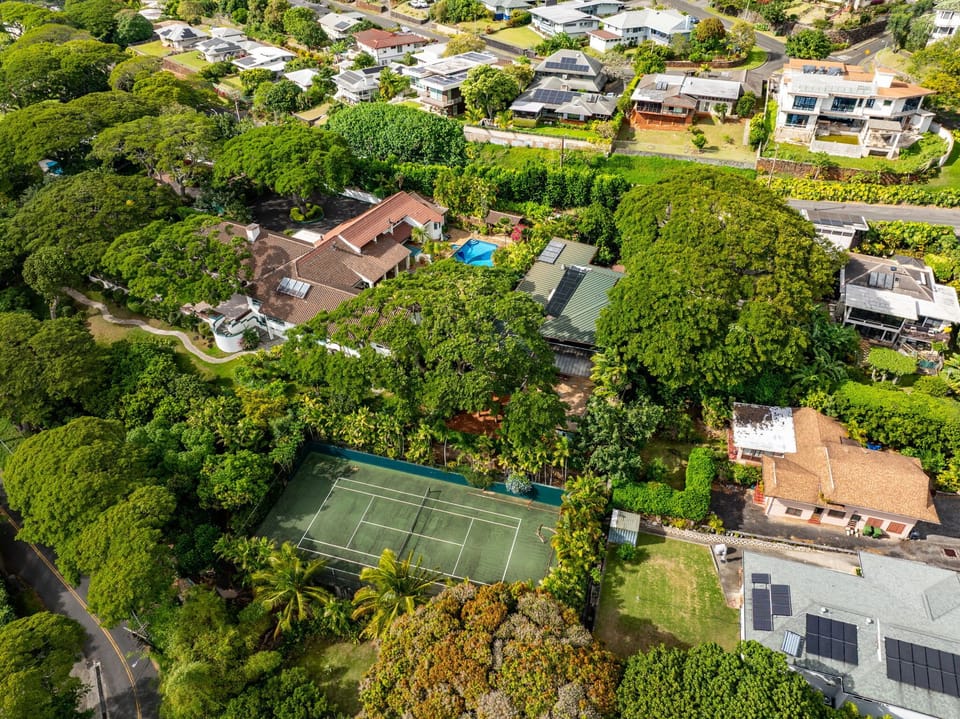Aerial view of a peaceful residential neighborhood featuring lush tropical vegetation, a tennis court, and well-maintained homes.