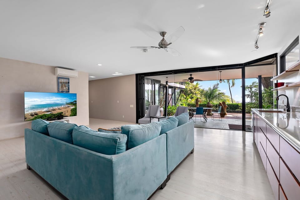 Relax in your open-concept living space where plush turquoise seating faces tropical gardens through floor-to-ceiling windows.