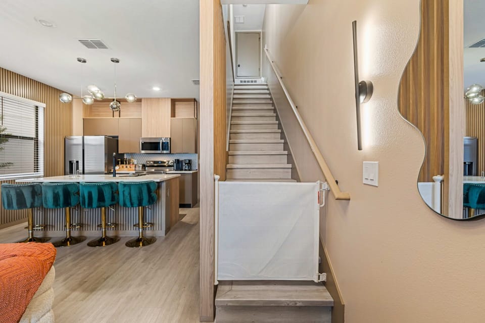Modern kitchen with teal bar stools and a staircase with a safety gate.
