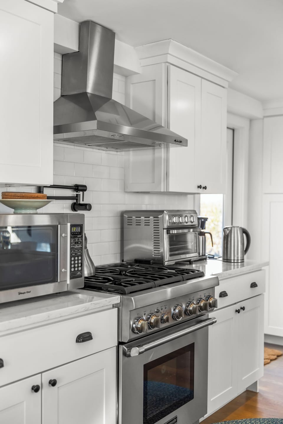 Bright chef’s kitchen with pro gas range, vent hood, and sleek white cabinetry.