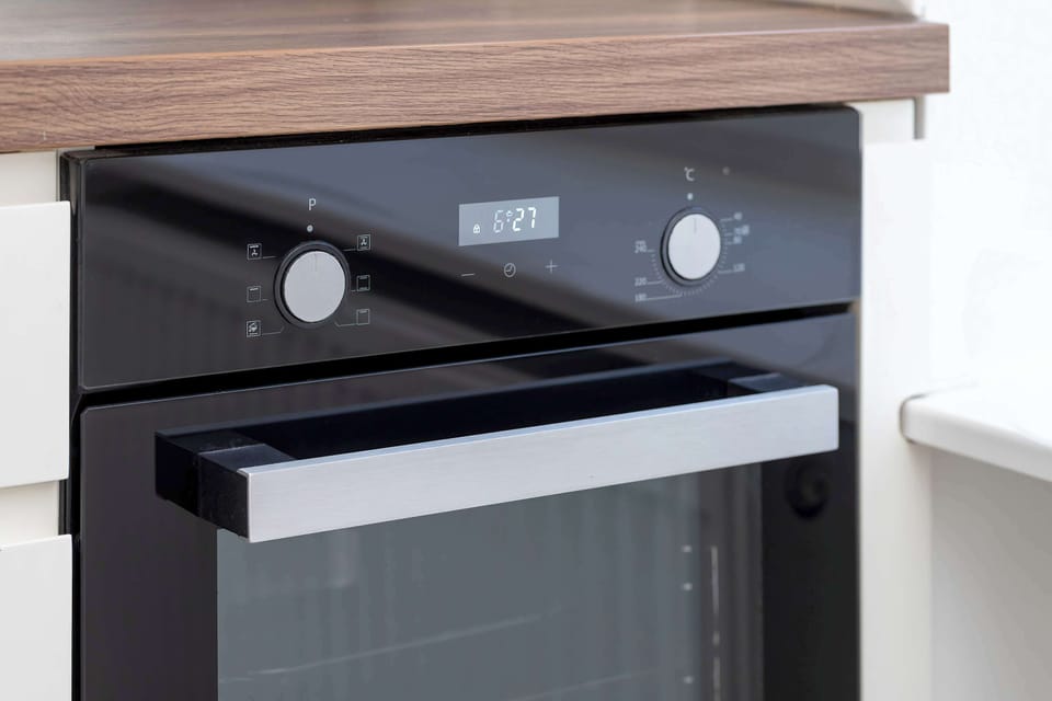 A detailed view focuses on a black and stainless steel built-in oven installed within a white kitchen cabinet.