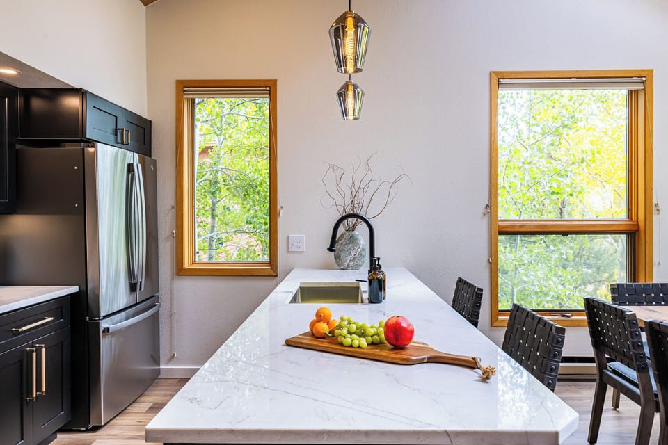 Kitchen — Modern Design Meets Function Modern chef’s kitchen with lake views, sleek black cabinetry, quartz counters, and stainless steel appliances. A great space to cook and gather after a day on the lake or exploring Rocky Mountain National Park.