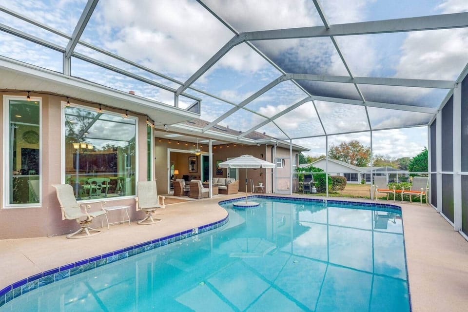 Screened pool oasis with covered lounge, in‑pool umbrella, and alfresco dining.