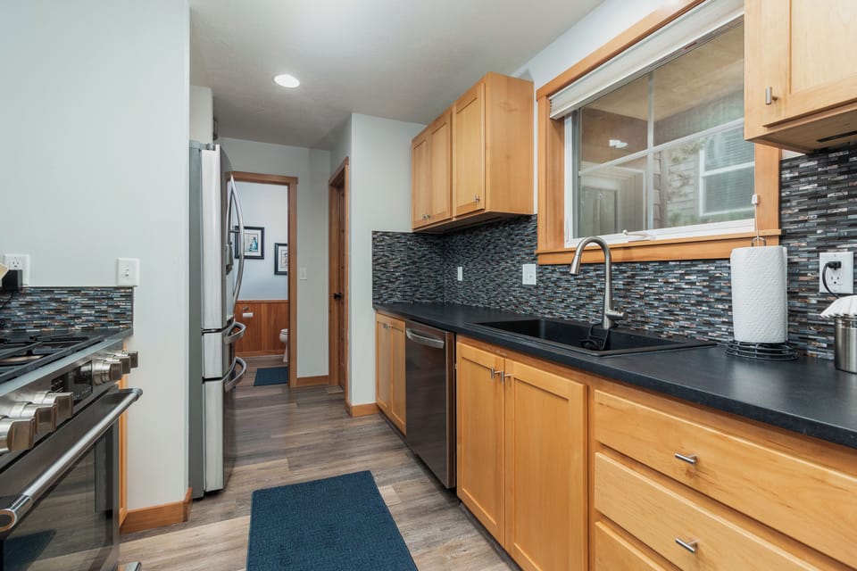 Cook your favorite meals in this modern kitchen featuring warm wood cabinets, sleek black countertops, and stylish mosaic backsplash.