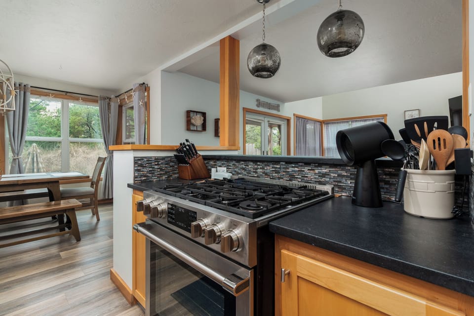 Cook memorable meals in your fully equipped kitchen, featuring granite countertops, stainless steel appliances, and elegant pendant lighting overlooking peaceful wooded views.