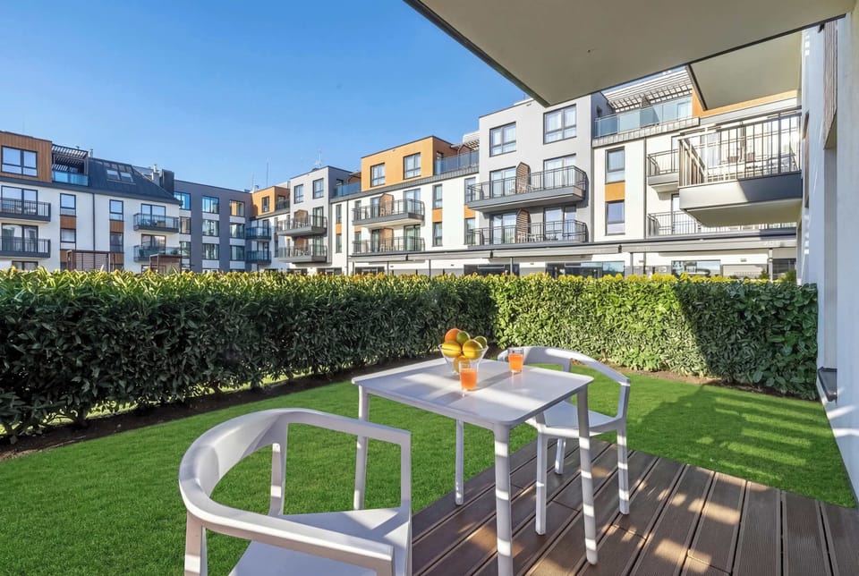 The outdoor seating area is positioned on artificial grass and wooden slats. It offers a quiet spot for morning coffee while overlooking the contemporary residential complex.