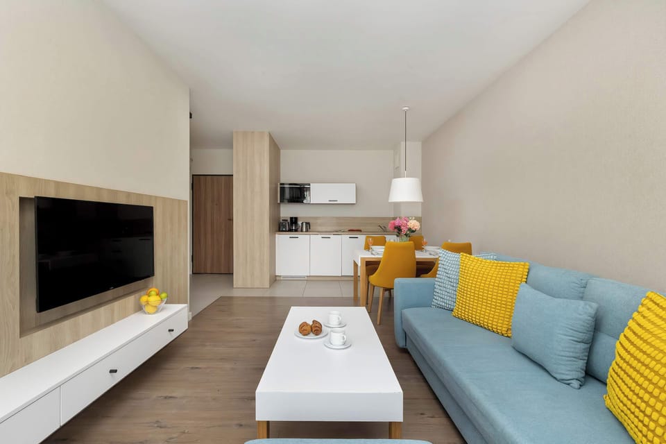 A wide perspective captures the long white TV console and the blue sofa arrangement. The minimalist decor and light-colored walls make the apartment feel modern and expansive.
