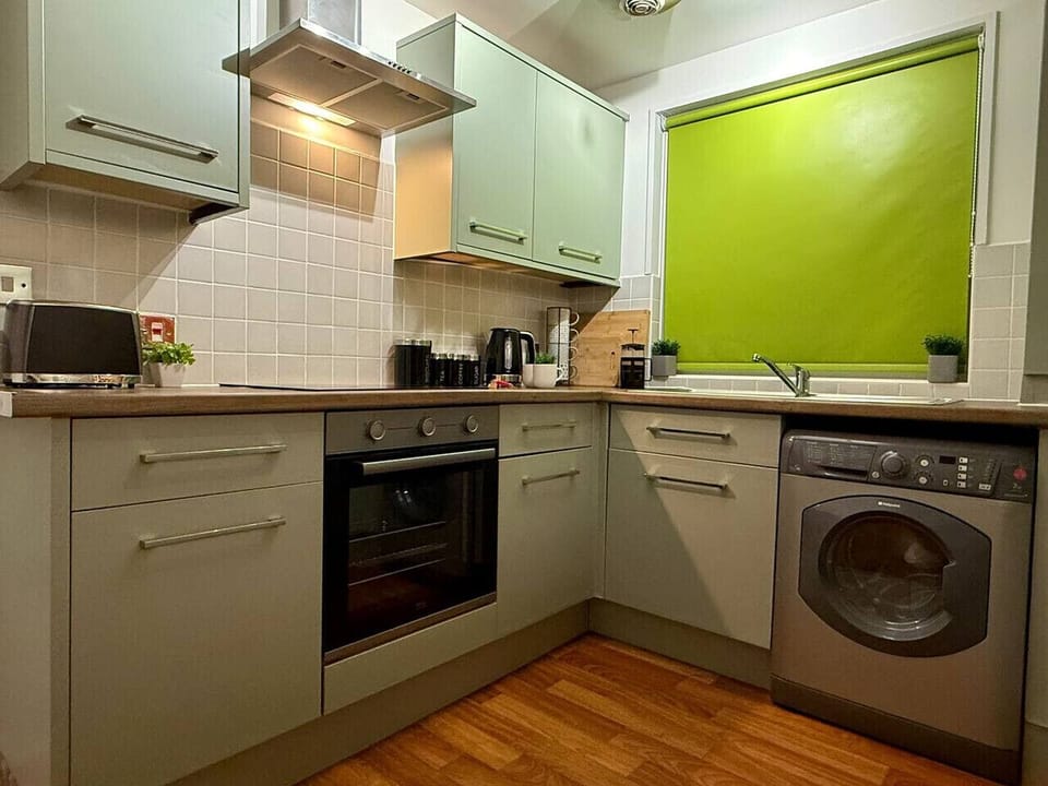 The fitted kitchen shows green wall and base units, a built-in oven, a washing machine, and a lime-green tiled splashback.