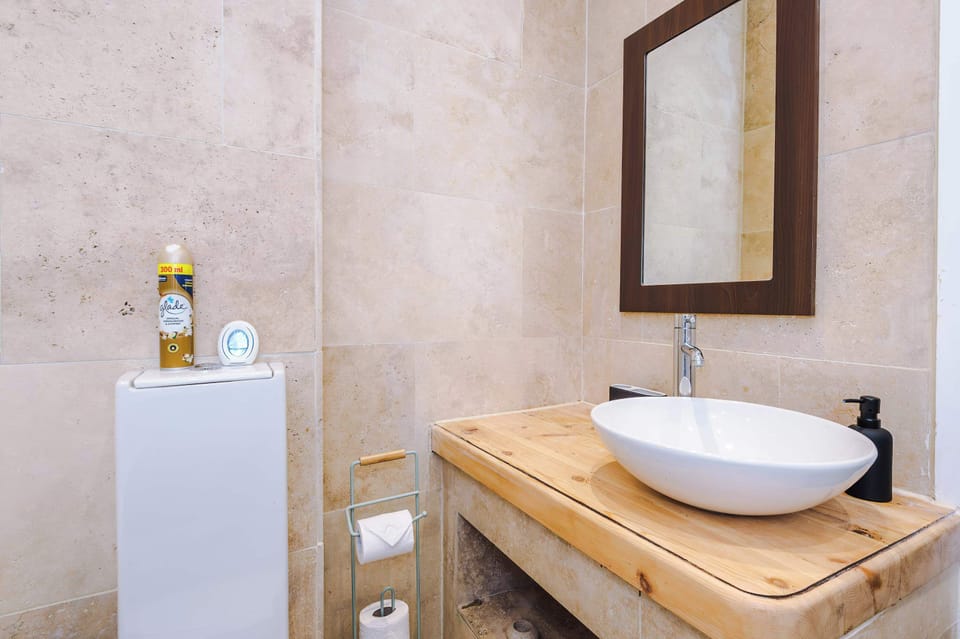 Modern full bathroom featuring a bathtub with glass screen, vessel sink on a wooden counter, and sleek wall-mounted faucet. Includes a toilet and built-in shelf—clean, minimalist design ideal for a relaxing soak or quick refresh.