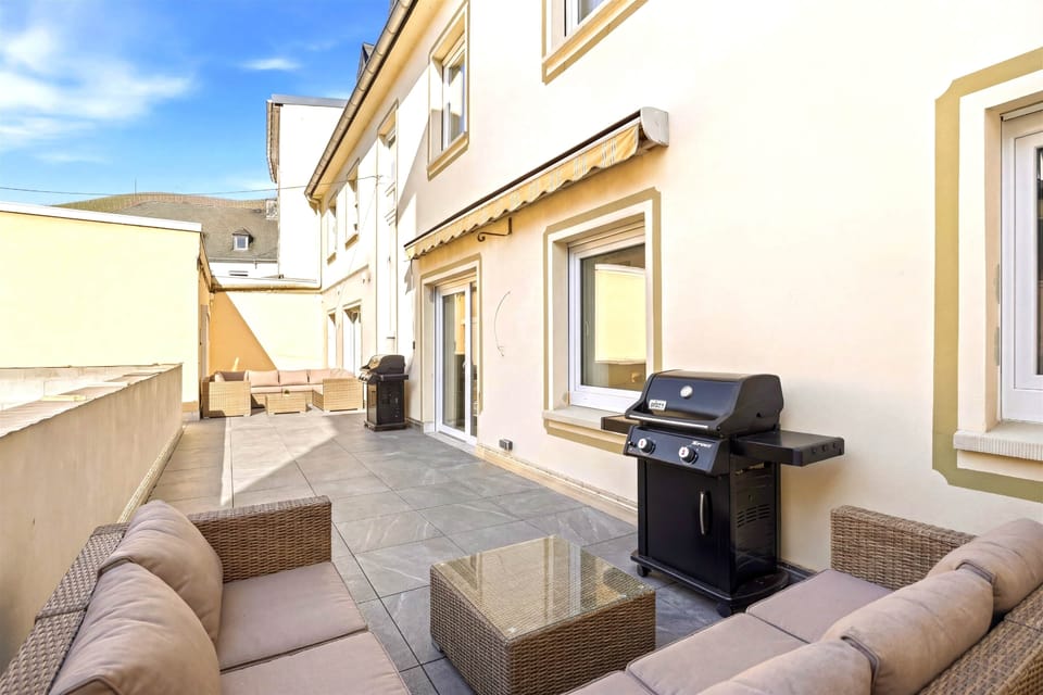 Gepflasterte Innenhofterrasse mit Rattan-Loungesessel, Gasgrill, Markise, helle Fassade.