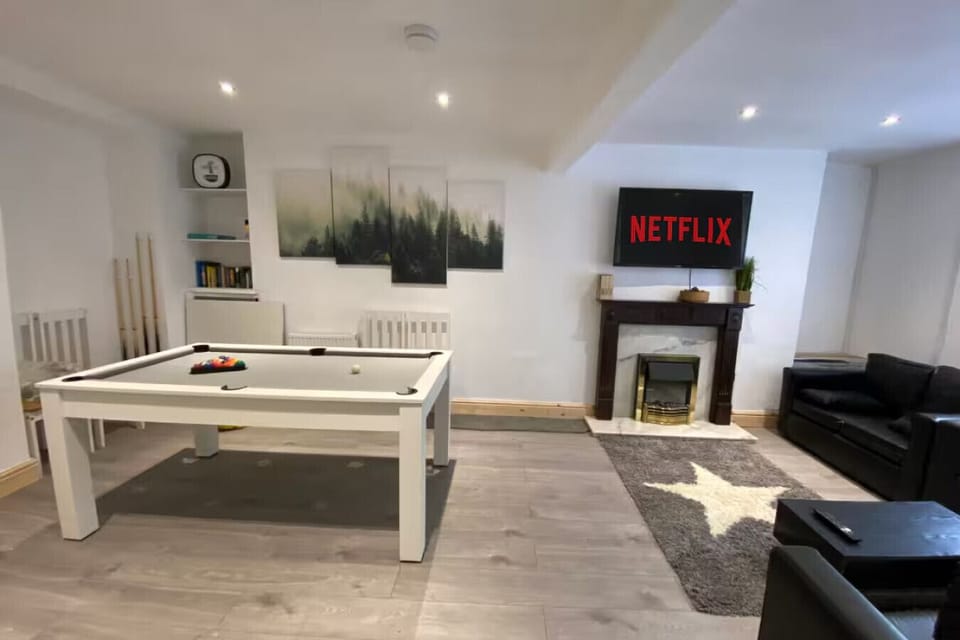 The living room showing the pool table in use, a fireplace with surround, black leather sofas, and a large wall-mounted Smart TV.